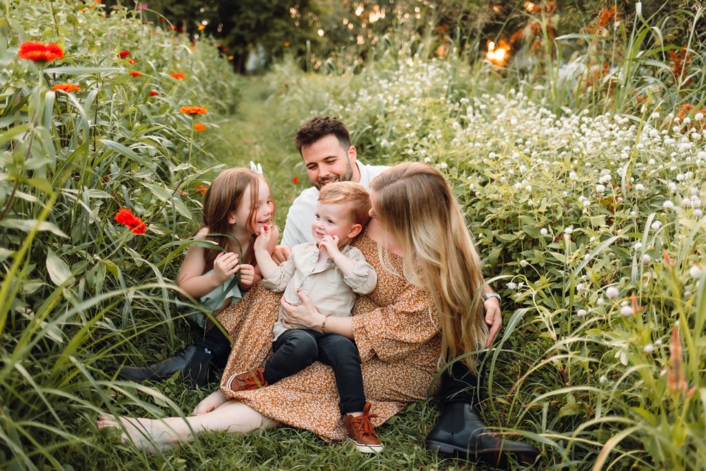 Family of four sitting in the grass surrounded by flowers snuggling and playing