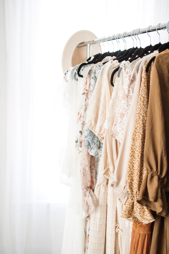 beautiful neutral colored dresses on a rack in front of a window in a bright white studio