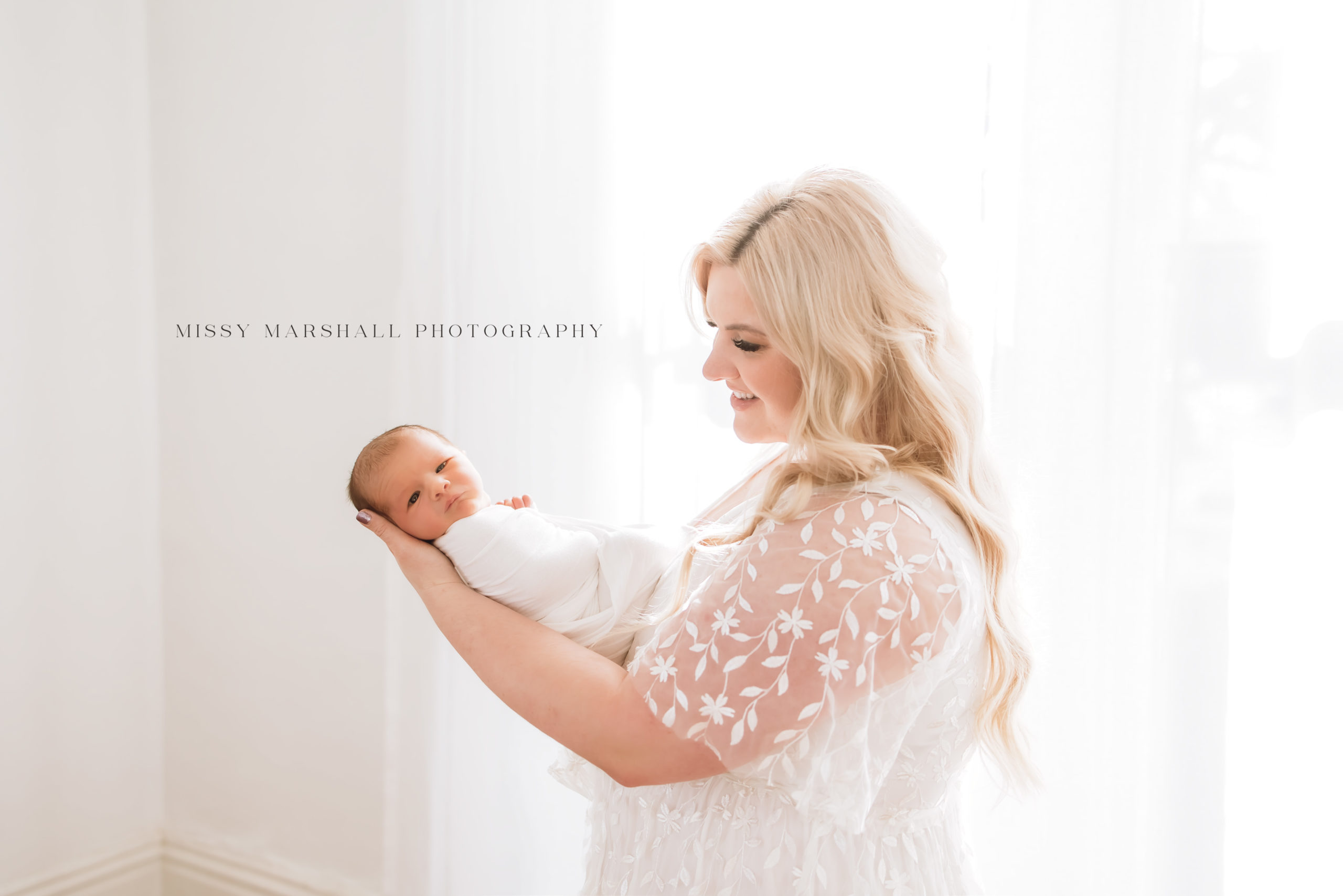 Louisville KY Newborn Photographer - portrait of beautiful mom holding her newborn baby all dressed in white in a bright, warm studio in Louisville Kentucky