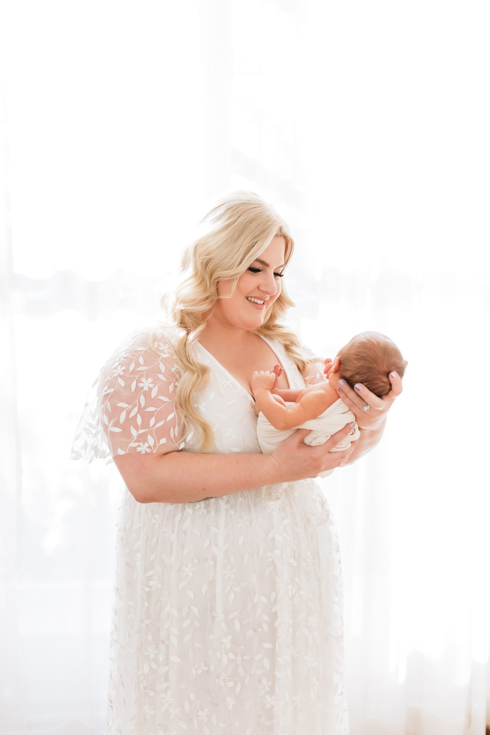 Louisville KY Newborn Photographer - portrait of beautiful mom holding her newborn baby all dressed in white in a bright, warm studio in Louisville Kentucky