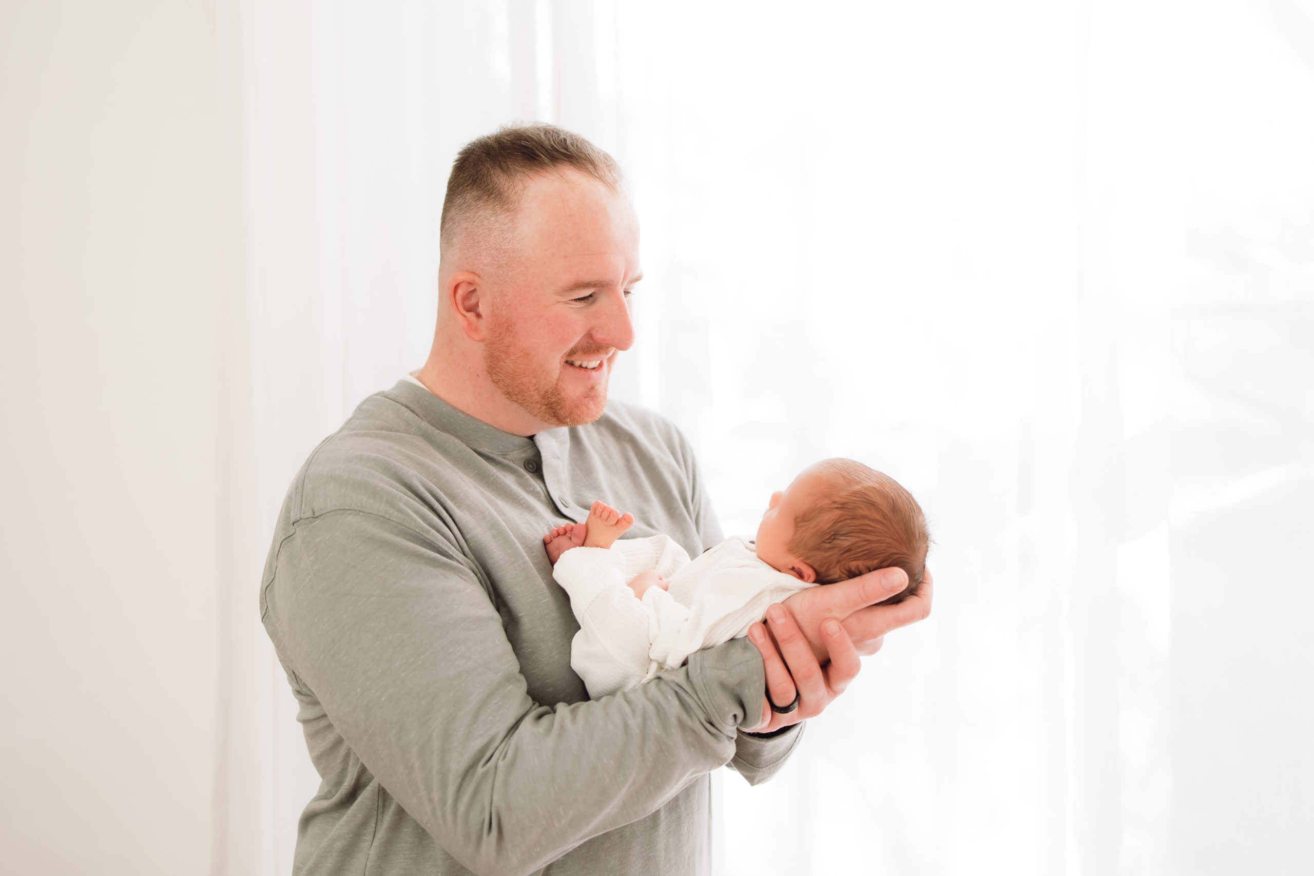 Portrait of proud dad holding his newborn baby all dressed in white in a bright, warm studio in Louisville Kentucky