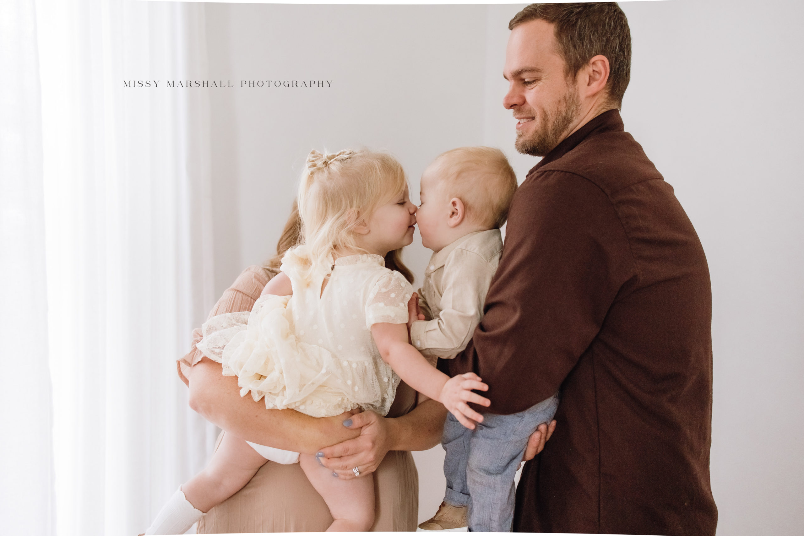 Louisville Newborn Photographers | Mom and dad holding their one year old baby and two year old toddler in a bright studio in Louisville KY taken by Missy Marshall Photography