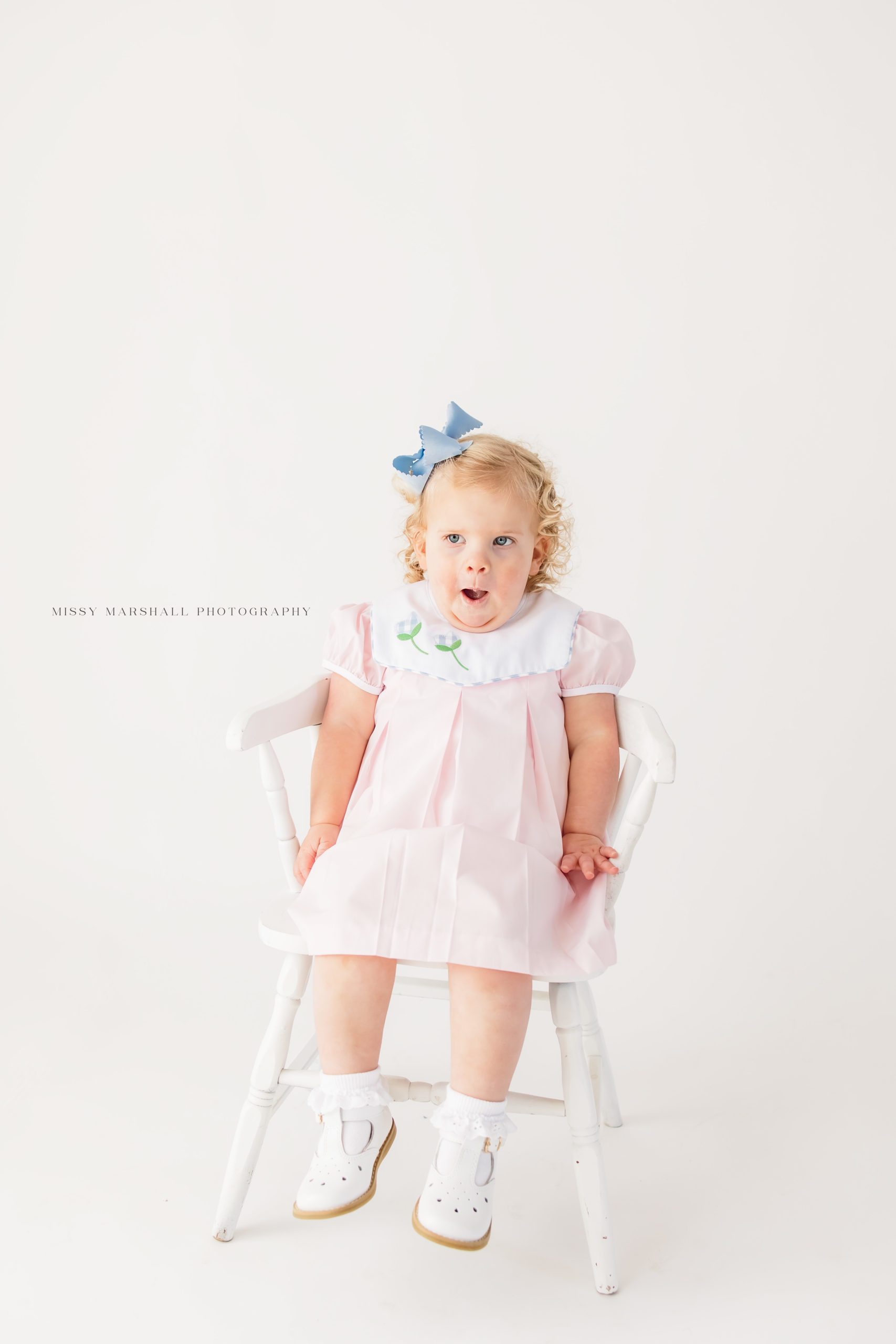 Baby girl making a funny face at a Louisville baby photographer with her hands in her lap during her milestone session