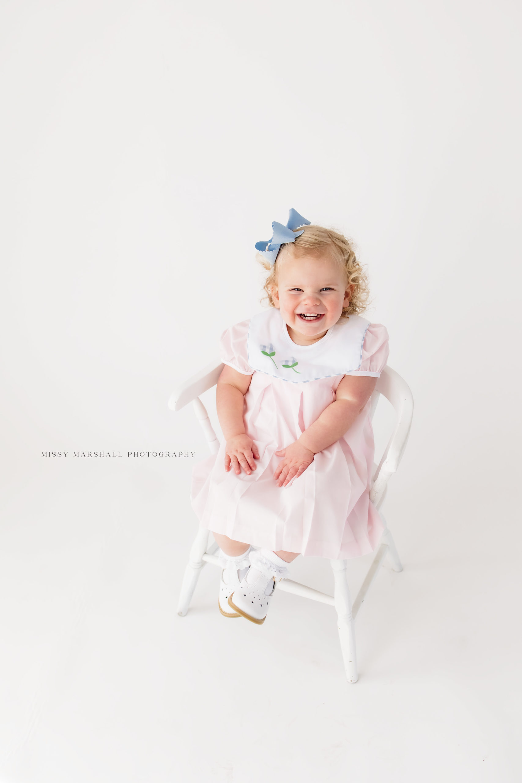 Baby girl smiling at a Louisville baby photographer with her hands in her lap during her milestone session