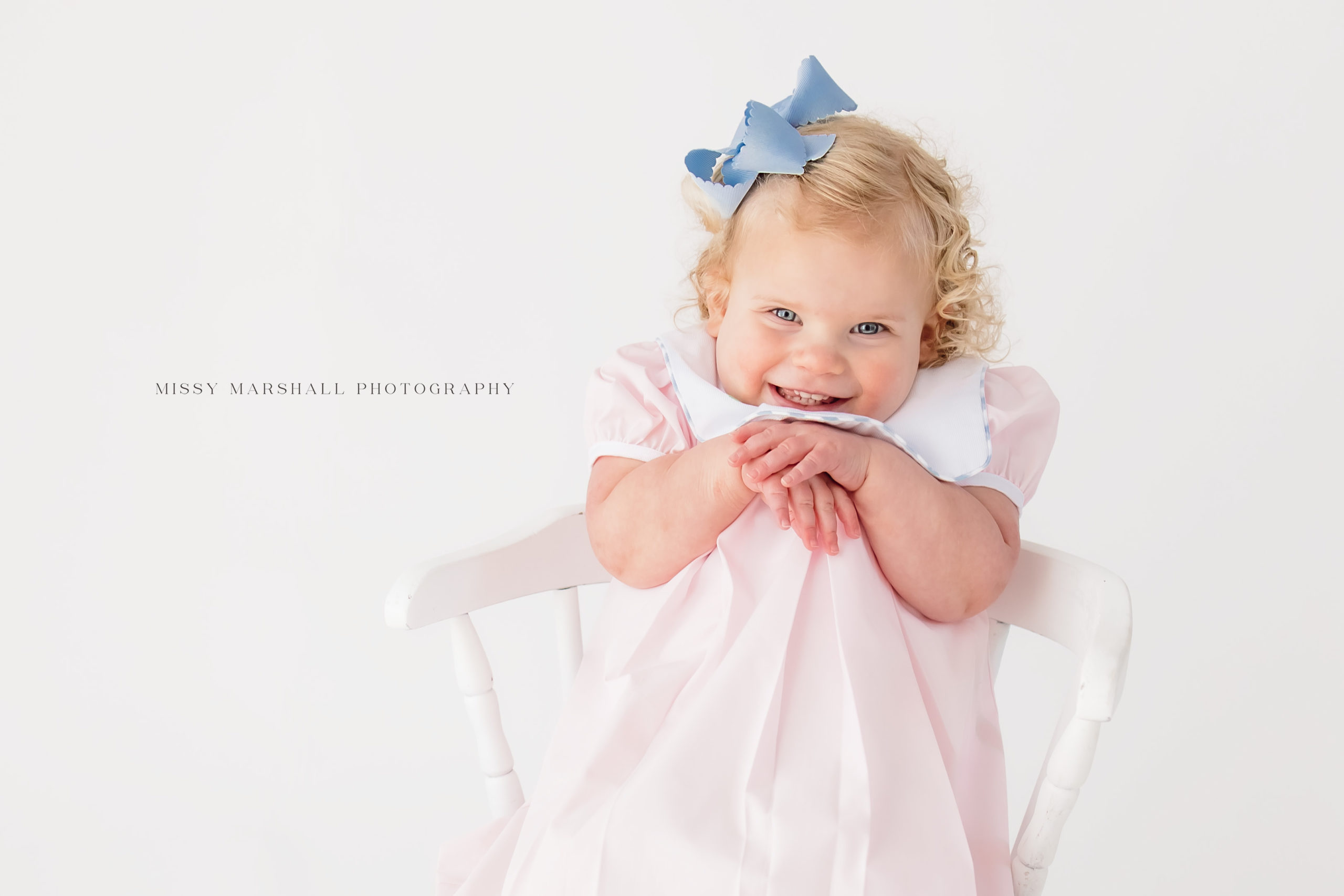 Close up of baby girl smiling at a Louisville baby photographer with her hands under her chin during her milestone session
