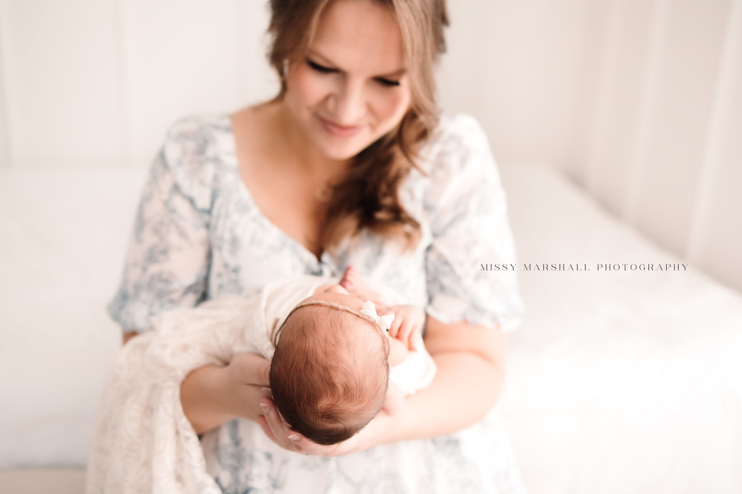 New mom smiling at her newborn baby in a bright white studio taken by a newborn photographer in Louisville