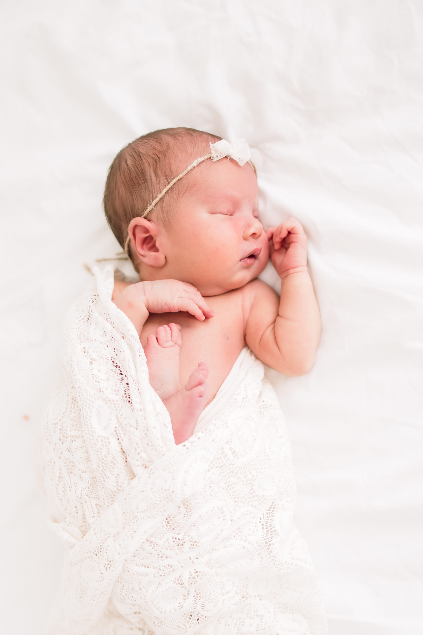 Newborn baby wearing a beautiful lace wrap and bow while sleeping in a bright white studio taken by a newborn photographer in Louisville
