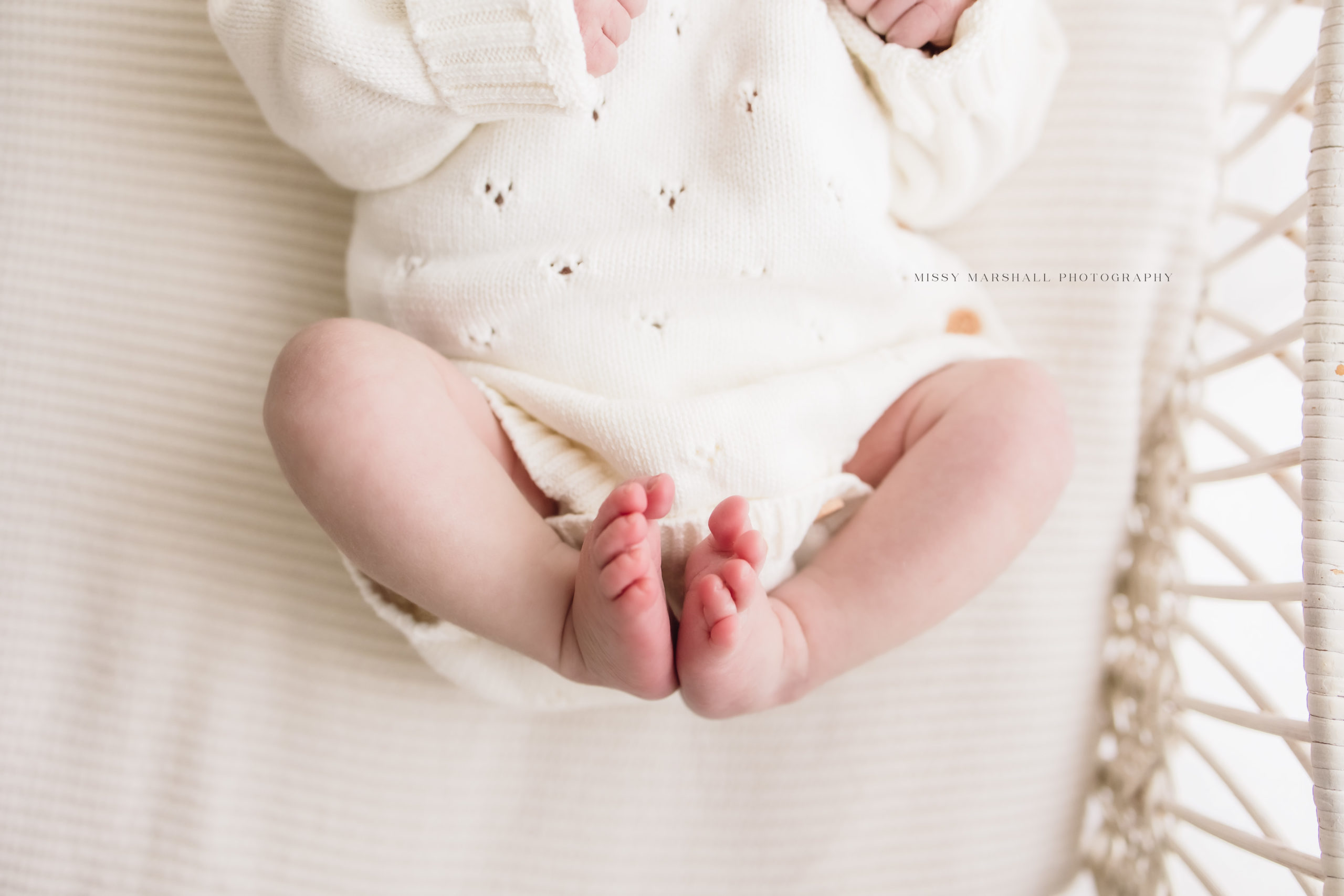 Newborn baby girl's little feet as she lays in a white bassinet wearing a white sweater taken by one of the newborn photographers in louisville
