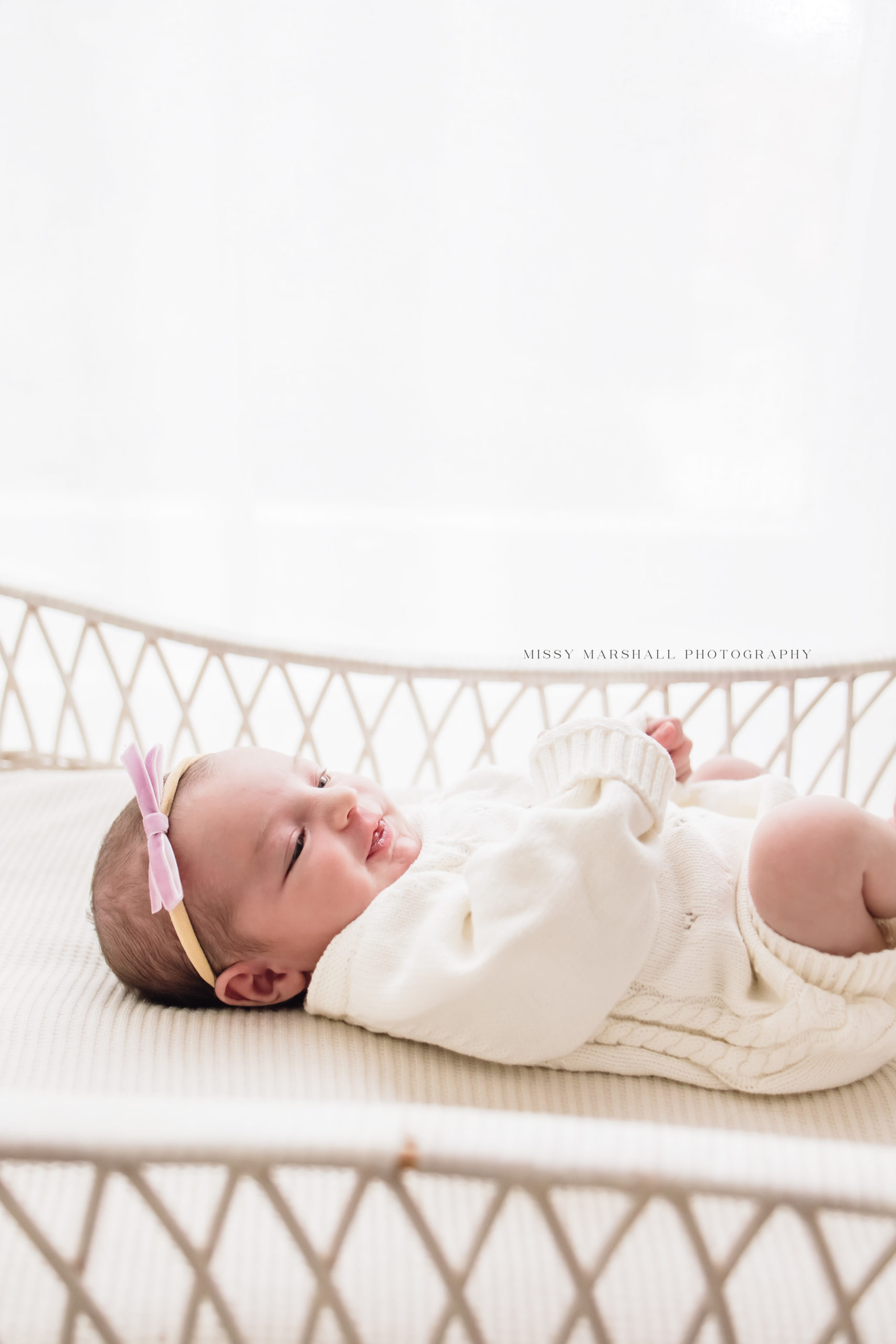 Newborn baby girl laying in a white bassinet taken by one of the newborn photographers in louisville
