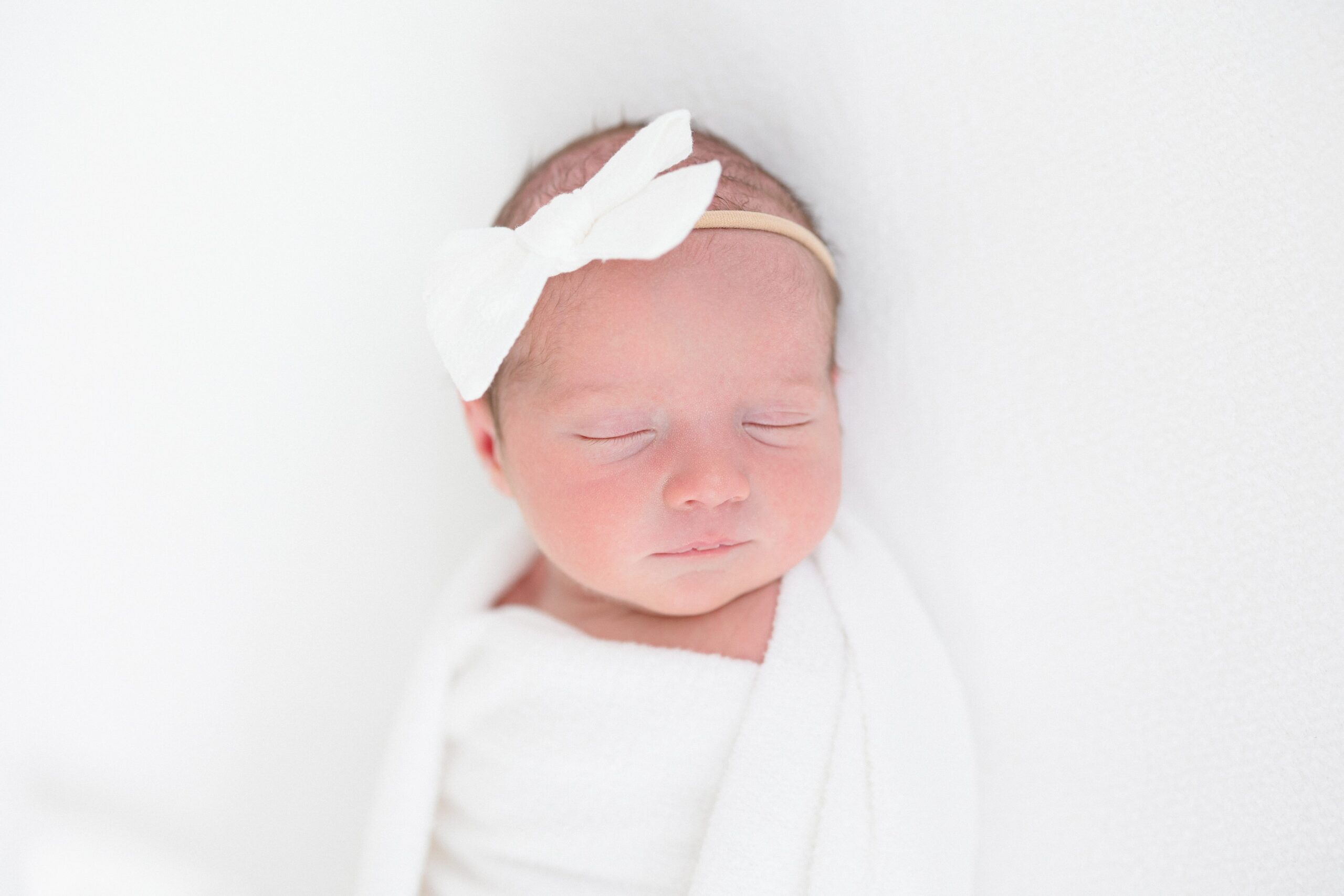 Newborn baby girl sleeping on a white backdrop during her newborn photo session