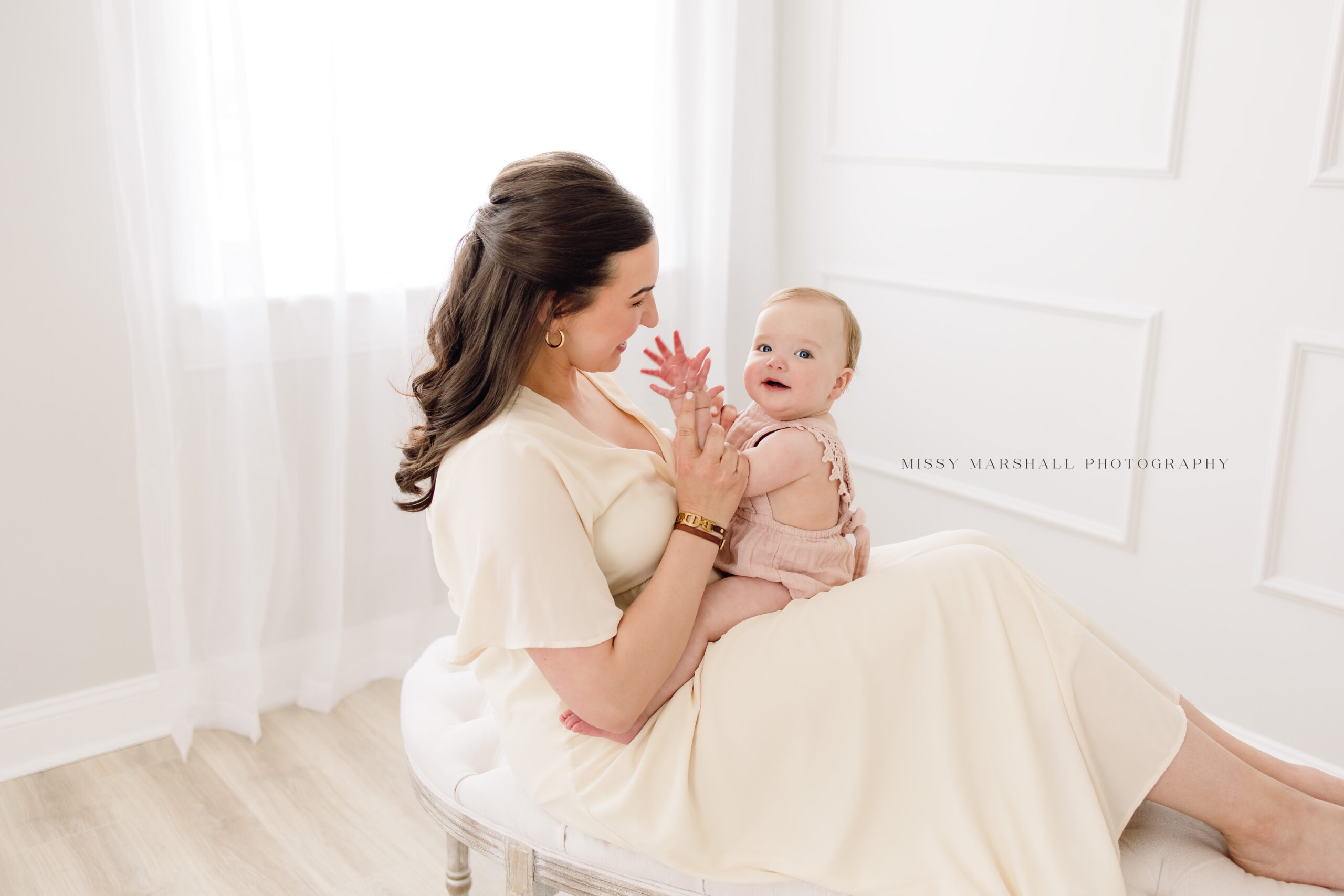 One year old baby girl sitting on her mom's lap clapping her hands and smiling at her first birthday milestone session