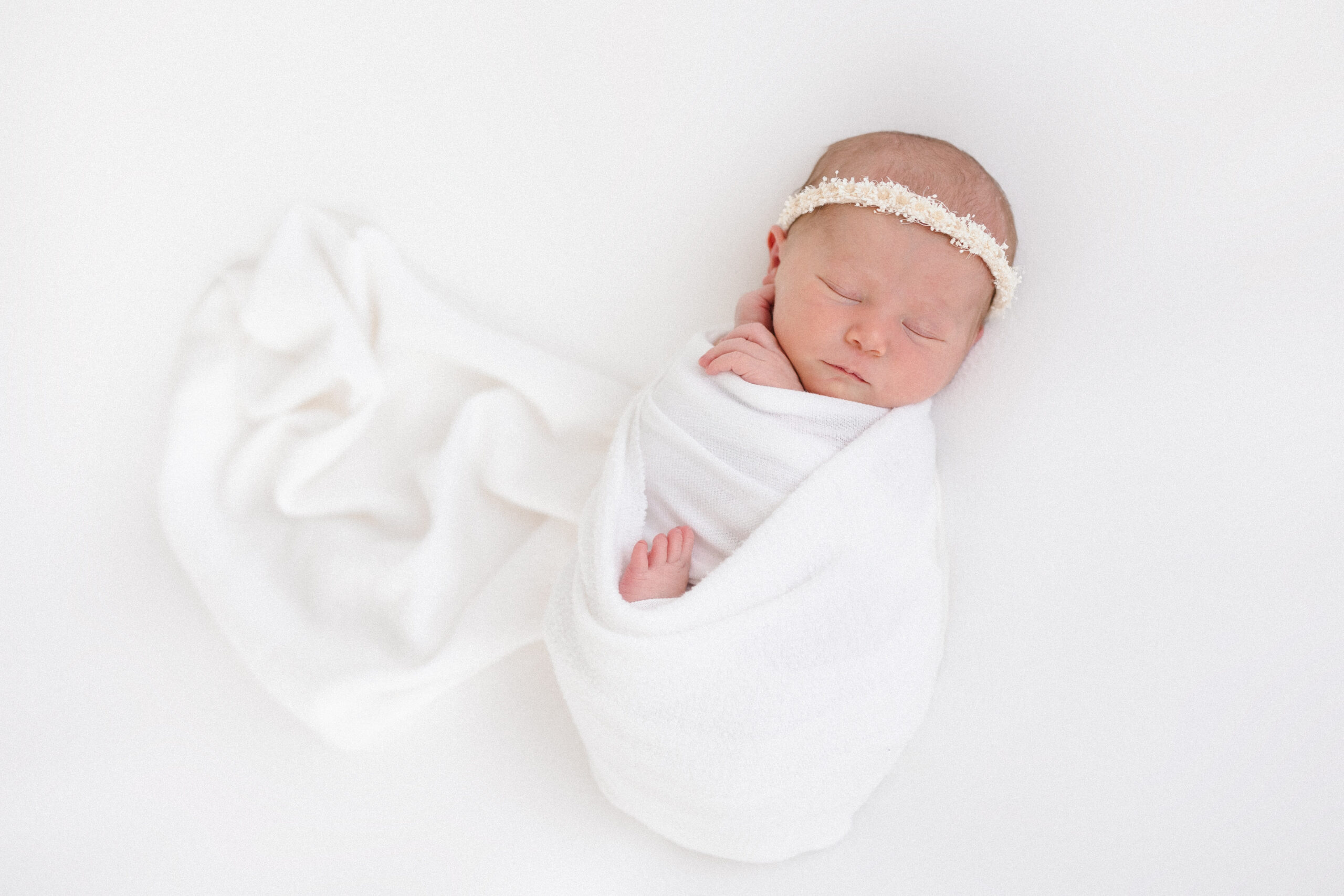 Baby girl swaddled in a white blanket as she sleeps with her hands by her face
