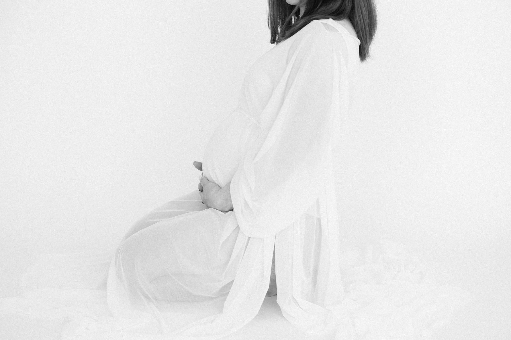 Black and white portrait of a pregnant mom kneeling on a white backdrop while she embraces her growing belly taken by Louisville KY maternity photographer missy marshall