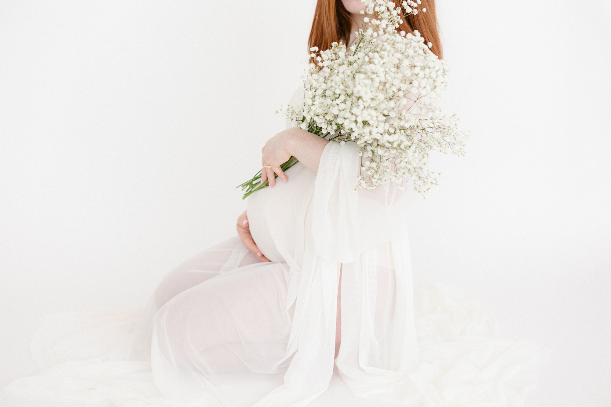 Portrait of a pregnant mom kneeling on a white backdrop while she holds white flowers taken by Louisville KY maternity photographer missy marshall