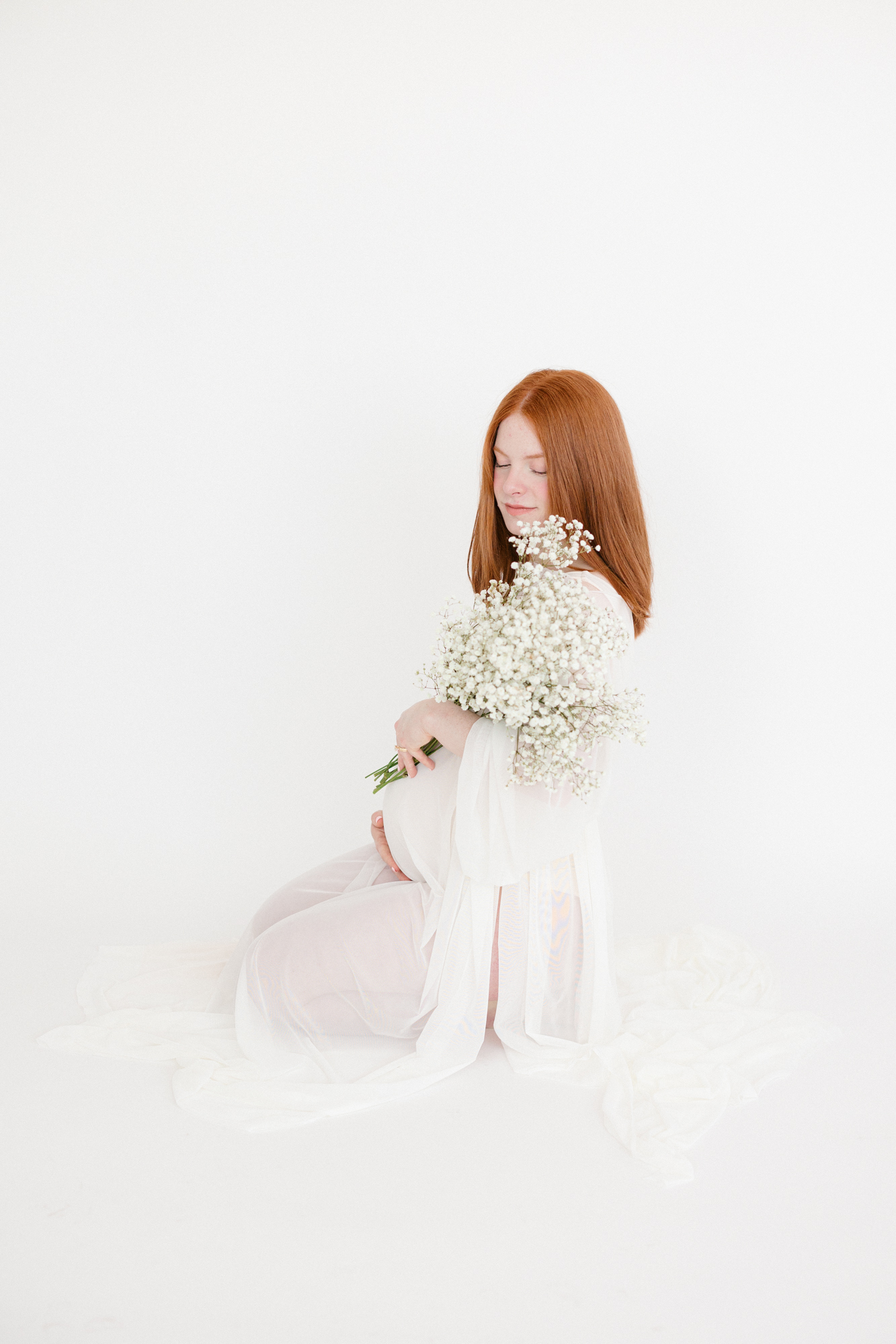 Portrait of a pregnant mom kneeling on a white backdrop holding flowers taken by Louisville KY maternity photographer missy marshall