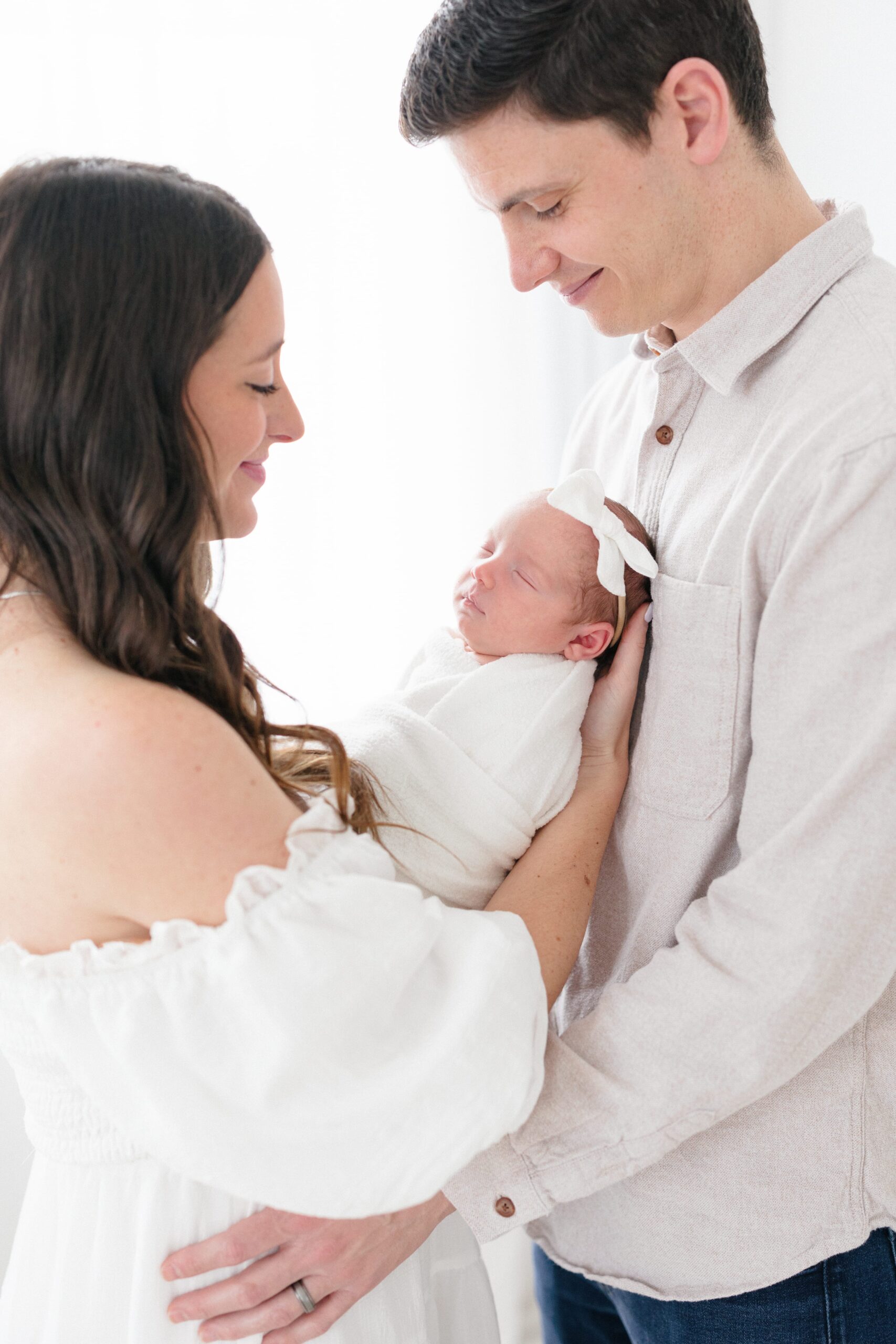 Portrait of a mom and dad holding their newborn baby girl and smiling at her in a Louisville KY newborn photography studio taken by missy marshall