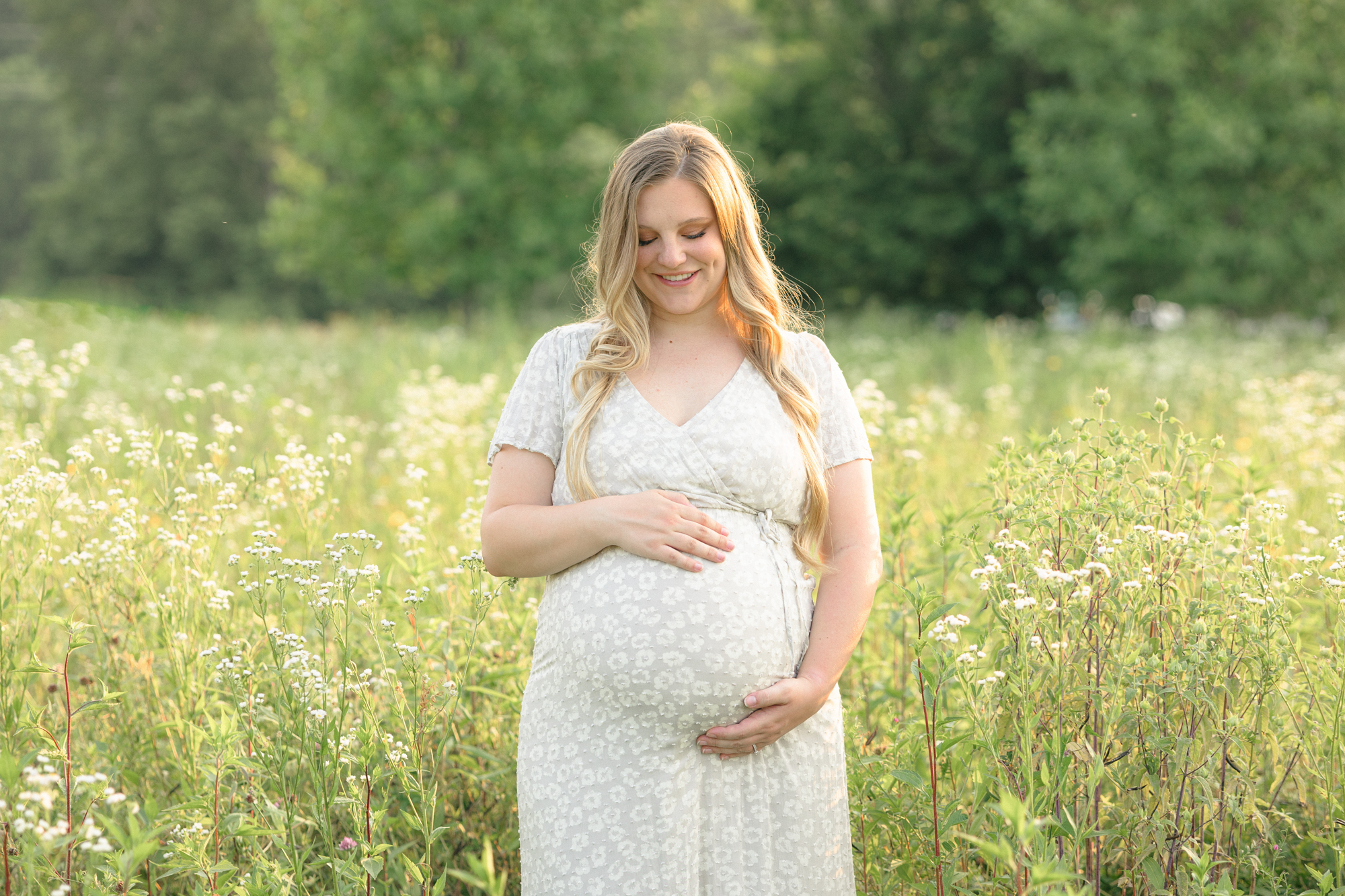 Pregnant mom holding her belly and smiling in a field of wildflowers during her Louisville maternity photography session